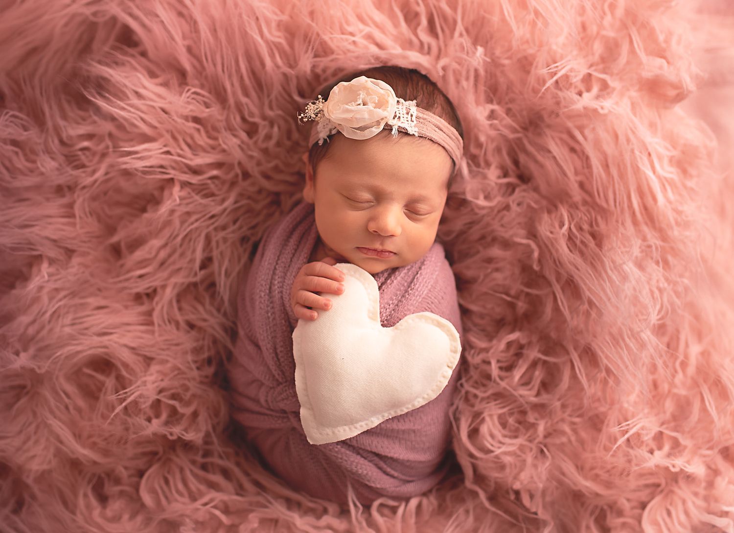 Baby girl snuggled and wrapped hold heart shaped fluffyin Alvin, Tx photography studio