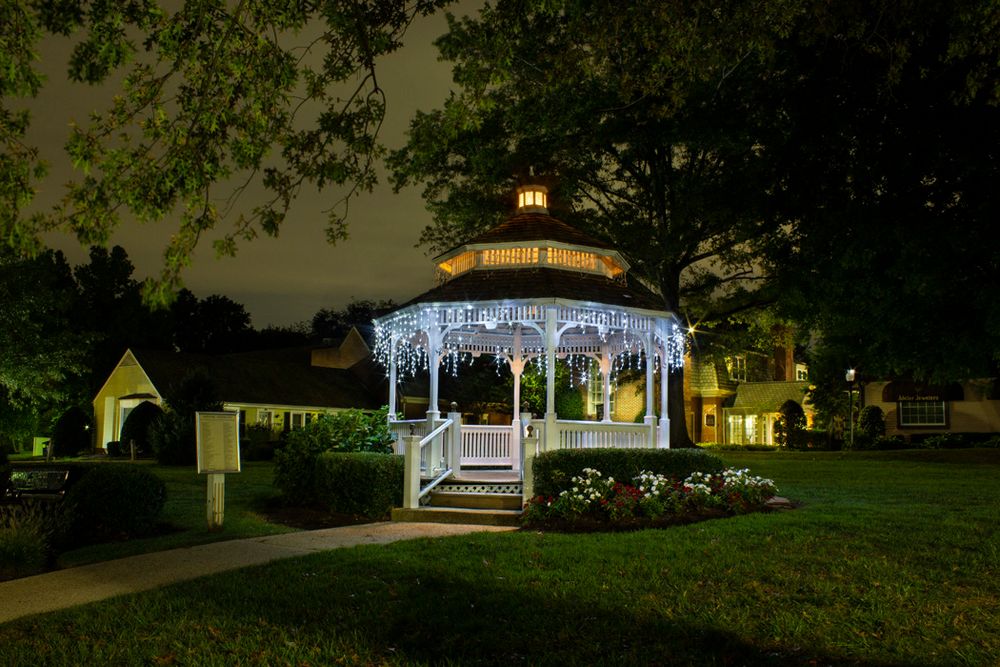 Illuminated white gazebo with string lights at night in a peaceful garden setting.