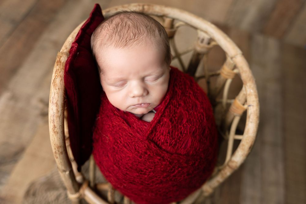 Peaceful sleeping newborn swaddled in red yarn inside vintage basket.