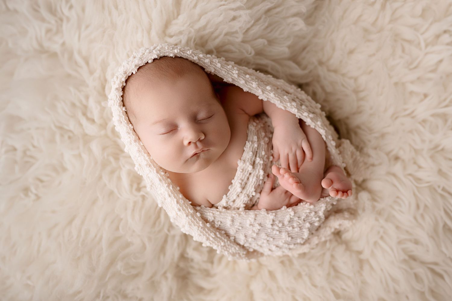 Professional newborn photography on plush white fur backdrop.