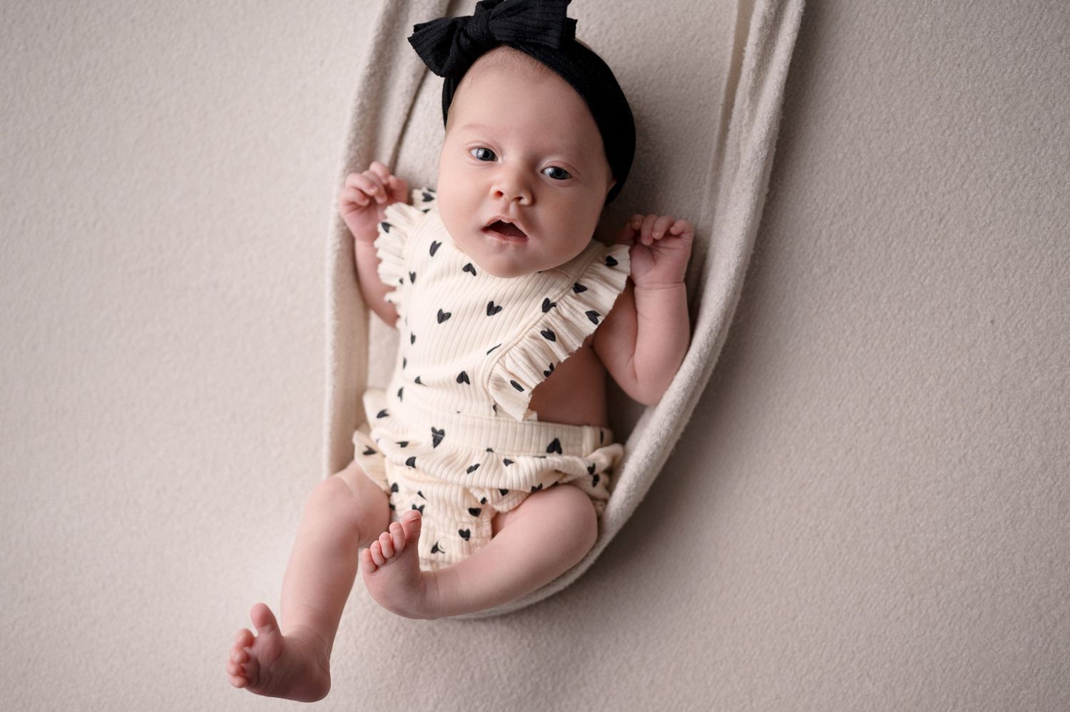 Studio portrait of baby in white ruffled outfit lying on plush backdrop.