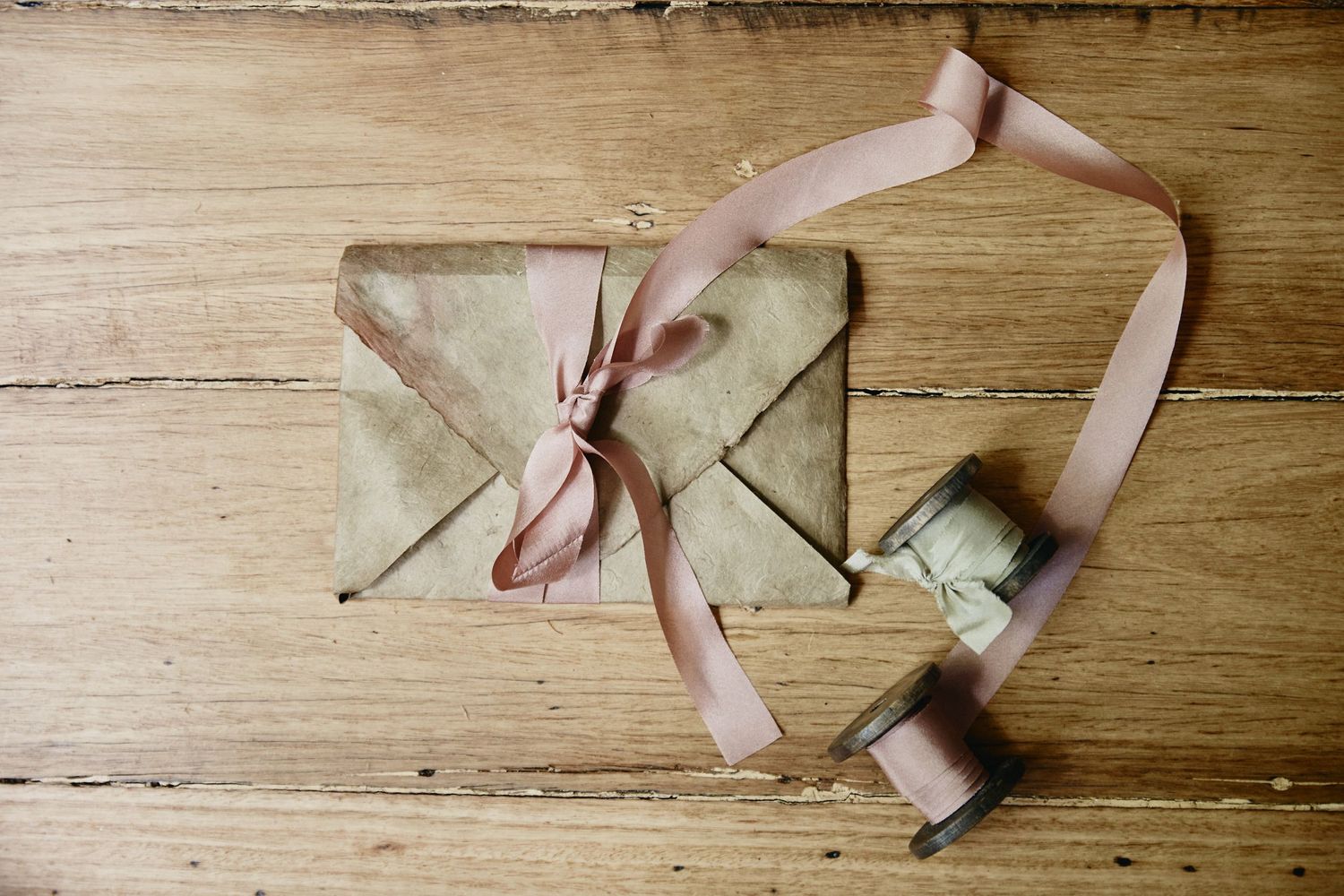 Rustic kraft paper envelopes tied with pink ribbon on wooden surface.