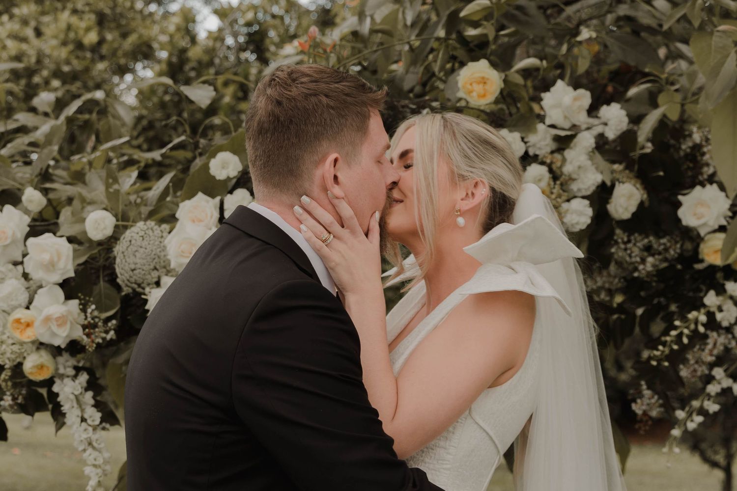 A romantic wedding kiss surrounded by white garden roses and greenery.