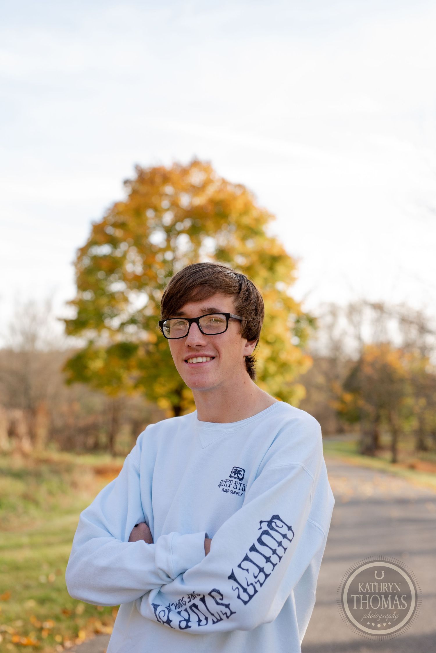 Person in white long-sleeve shirt poses confidently against autumn foliage background.