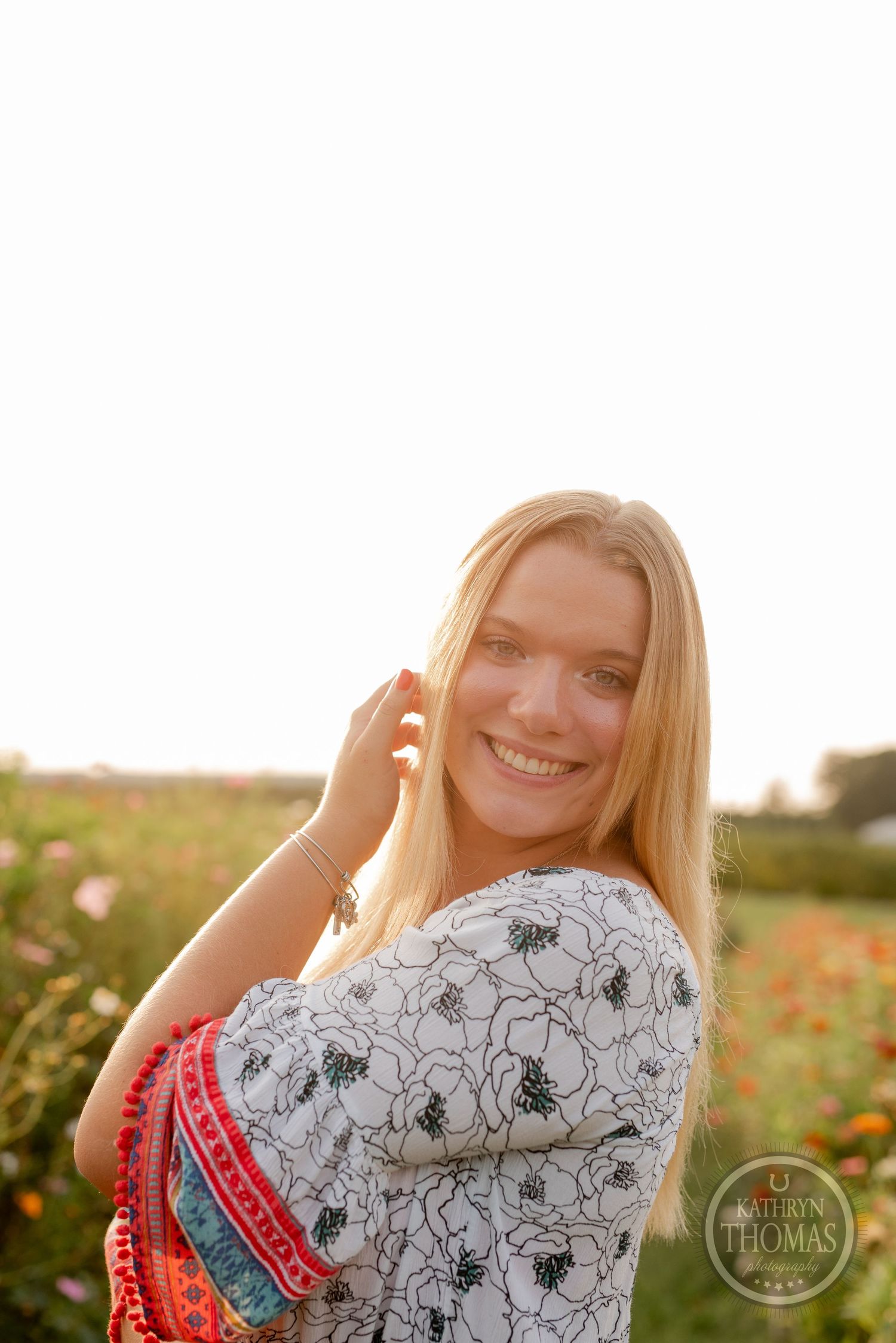 Bright portrait in a floral print top with flowing hair against a sunset wildflower field.