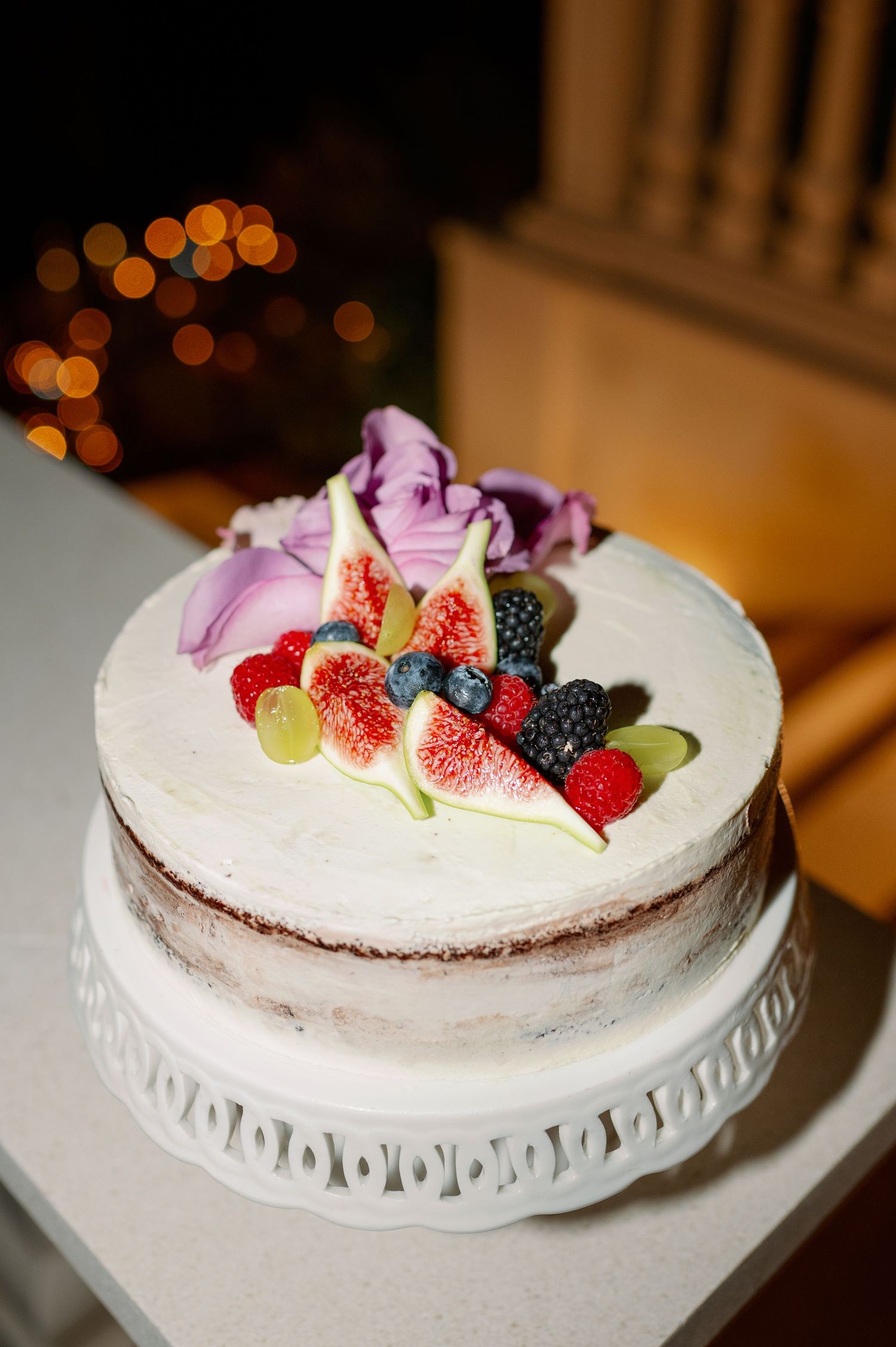 Beautiful wedding cake decorated with fresh fruit and pink flowers on white stand.