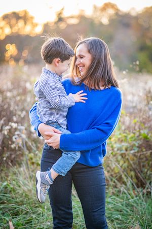 A DC mother stands in a field gazing lovingly at her toddler son whom she holds in her arms as the sun sets behind them.
