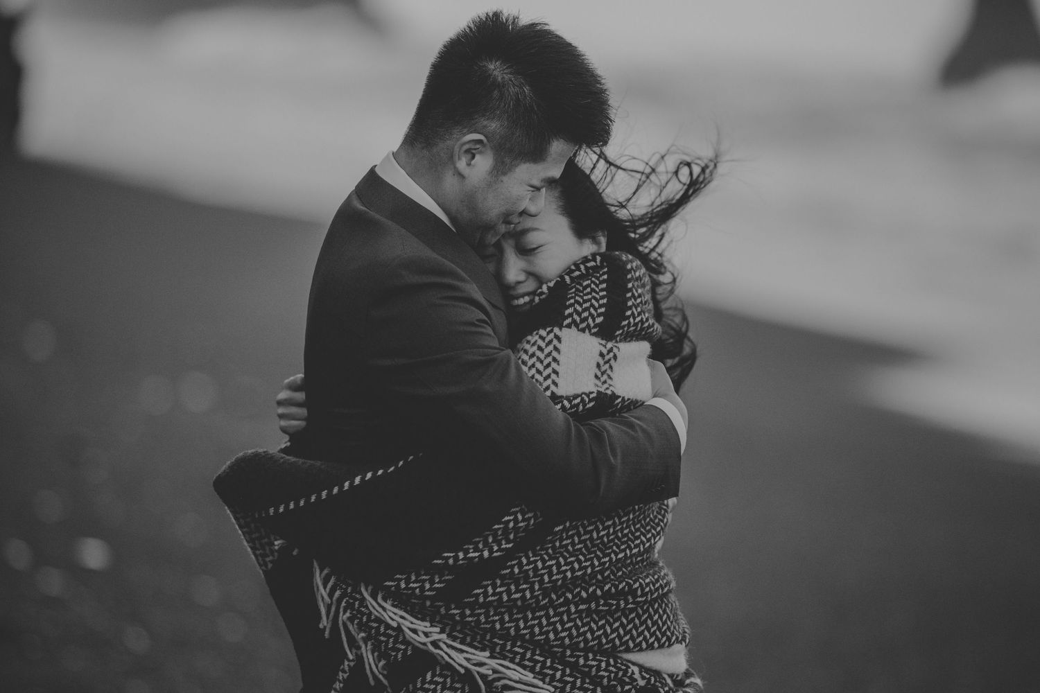 A tender black and white moment shared between a couple wrapped in a patterned blanket.