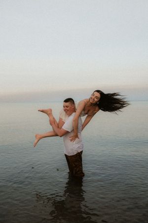 Two people playing and splashing in calm ocean waters at sunset.