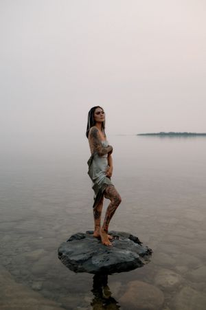 Person sitting on a large rock in shallow water during sunset.