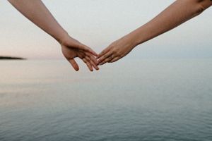 Hands reaching across the ocean horizon at sunset.