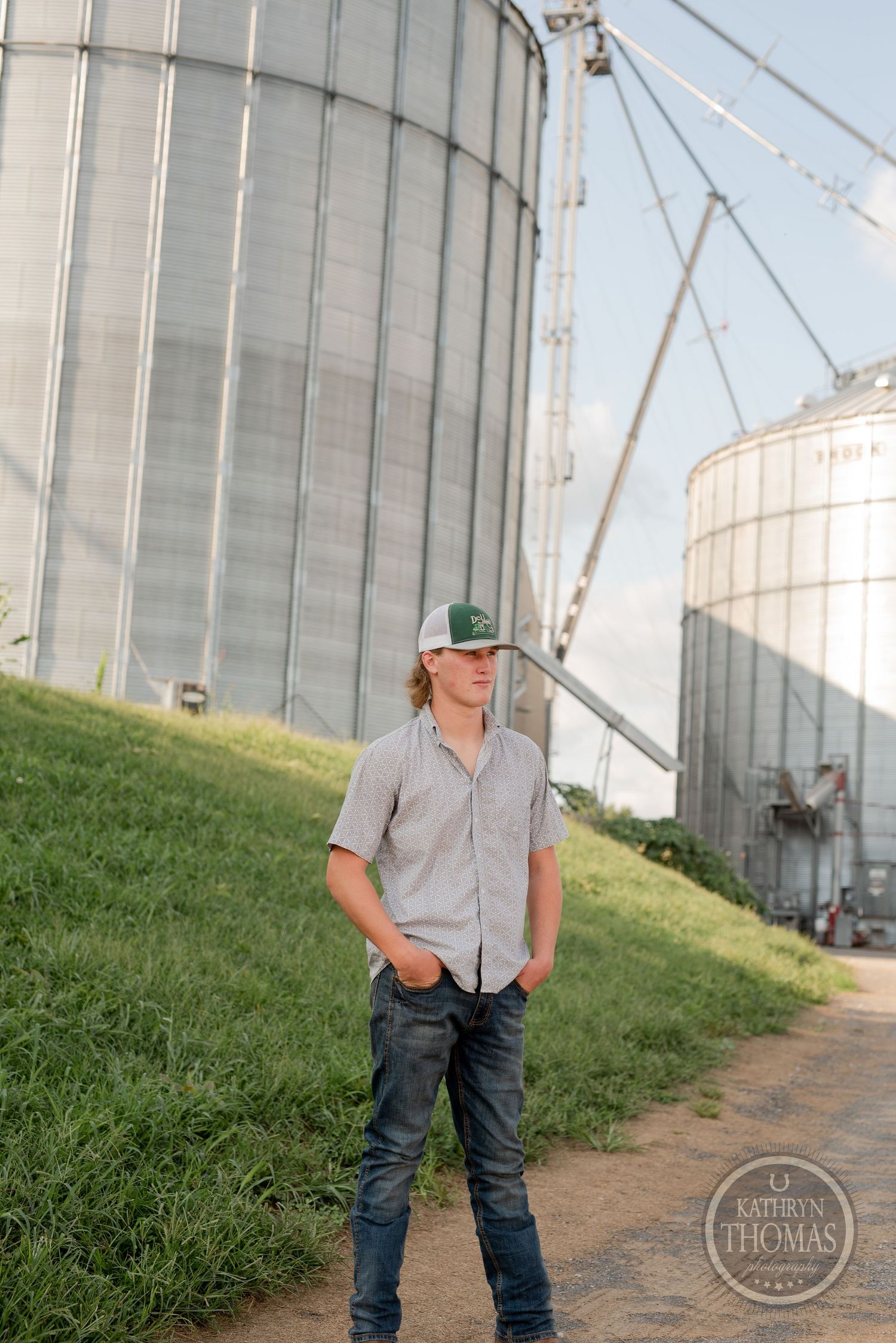Agricultural scene featuring large metal grain silos and grassy slope on a sunny day.