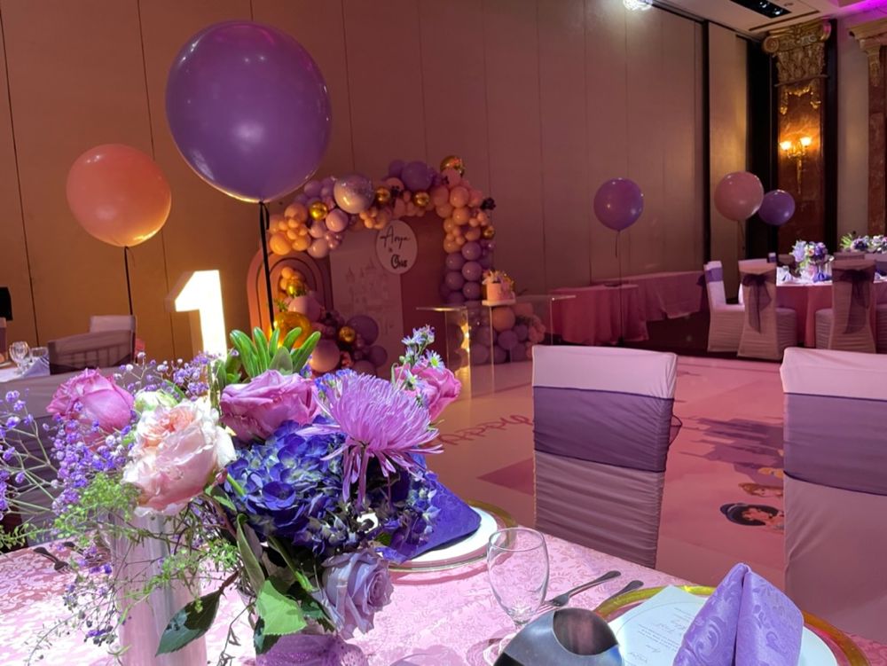 Guest table setup for a birthday party with pink and purple flowers and balloons, and cutlery