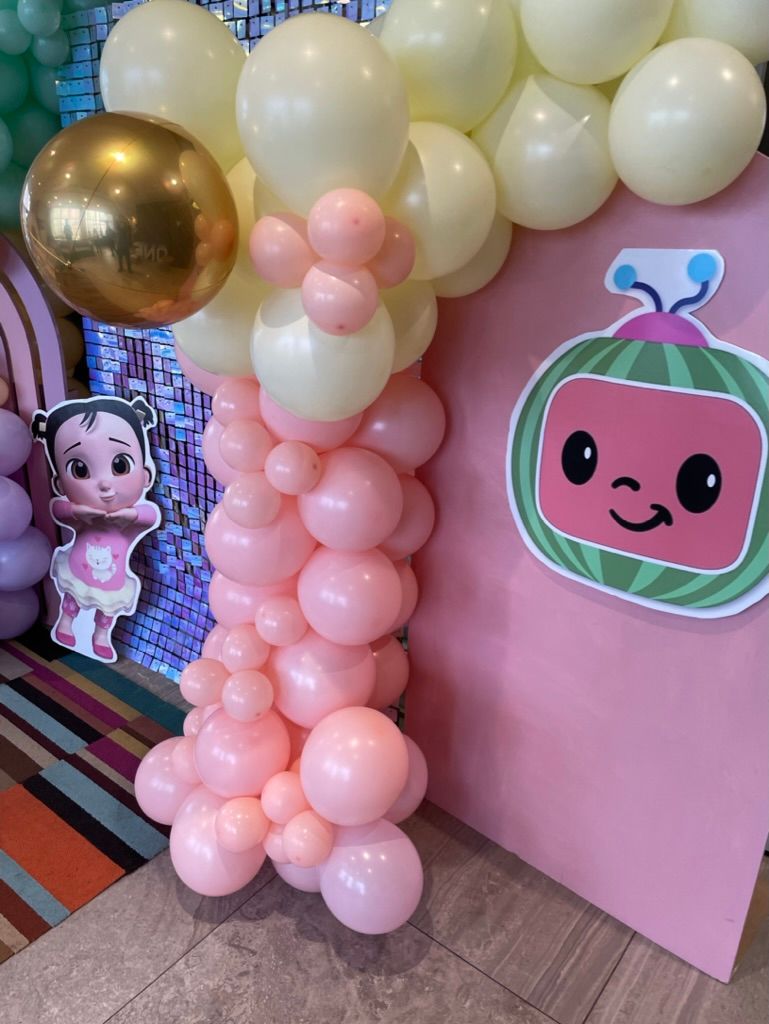 Cocomelon themed backdrop with pink and yellow balloons and character cutout