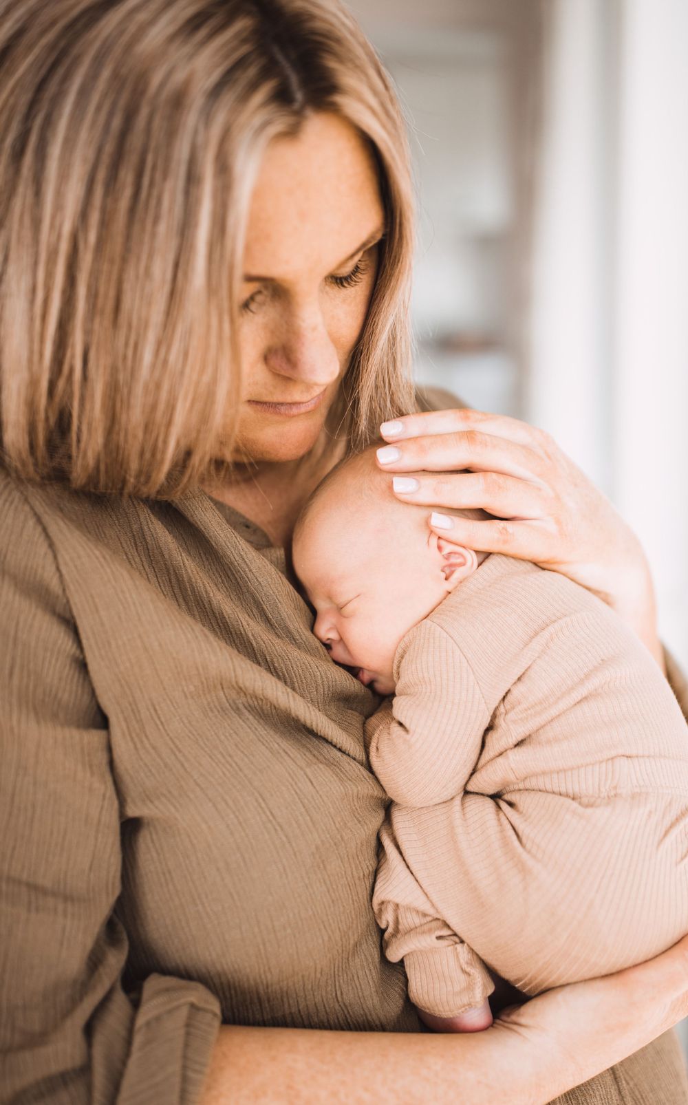 A tender moment between parent and baby in soft neutral tones showing gentle embrace and connection.