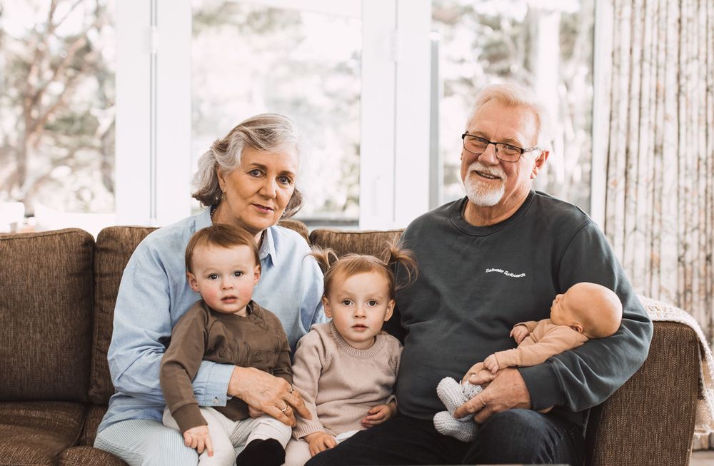 Multi-generational family relaxing together on a cozy brown sofa.