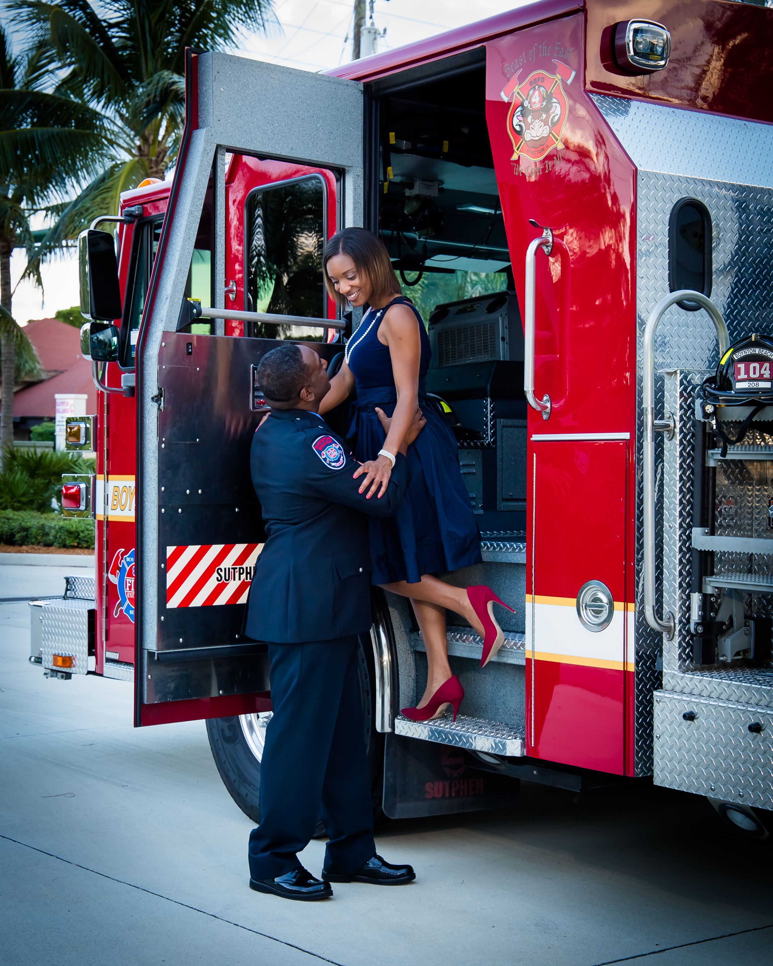 A person in a blue dress stands on a fire truck while another person assists below.