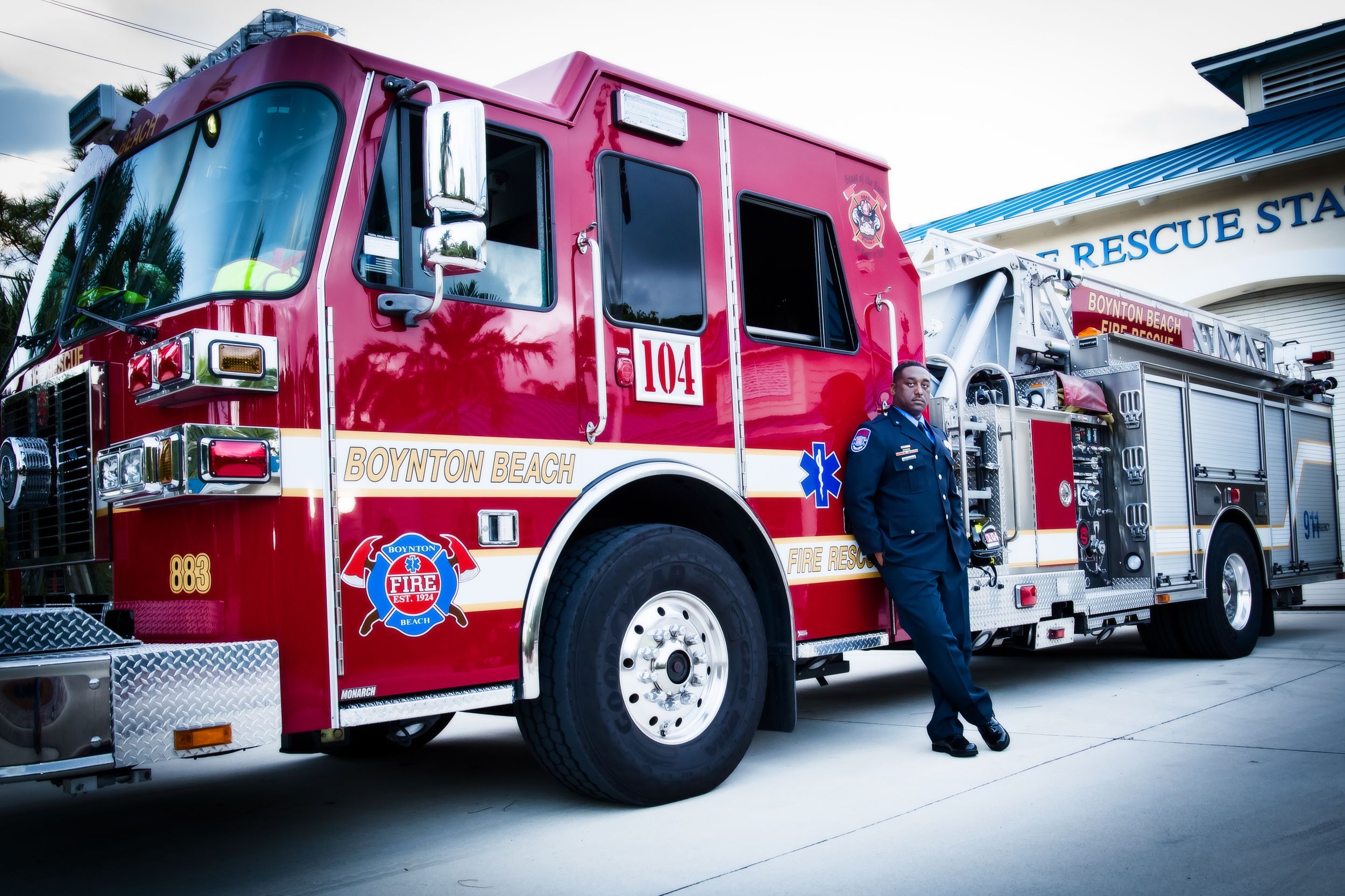 A person in uniform stands beside a red fire engine at a station.