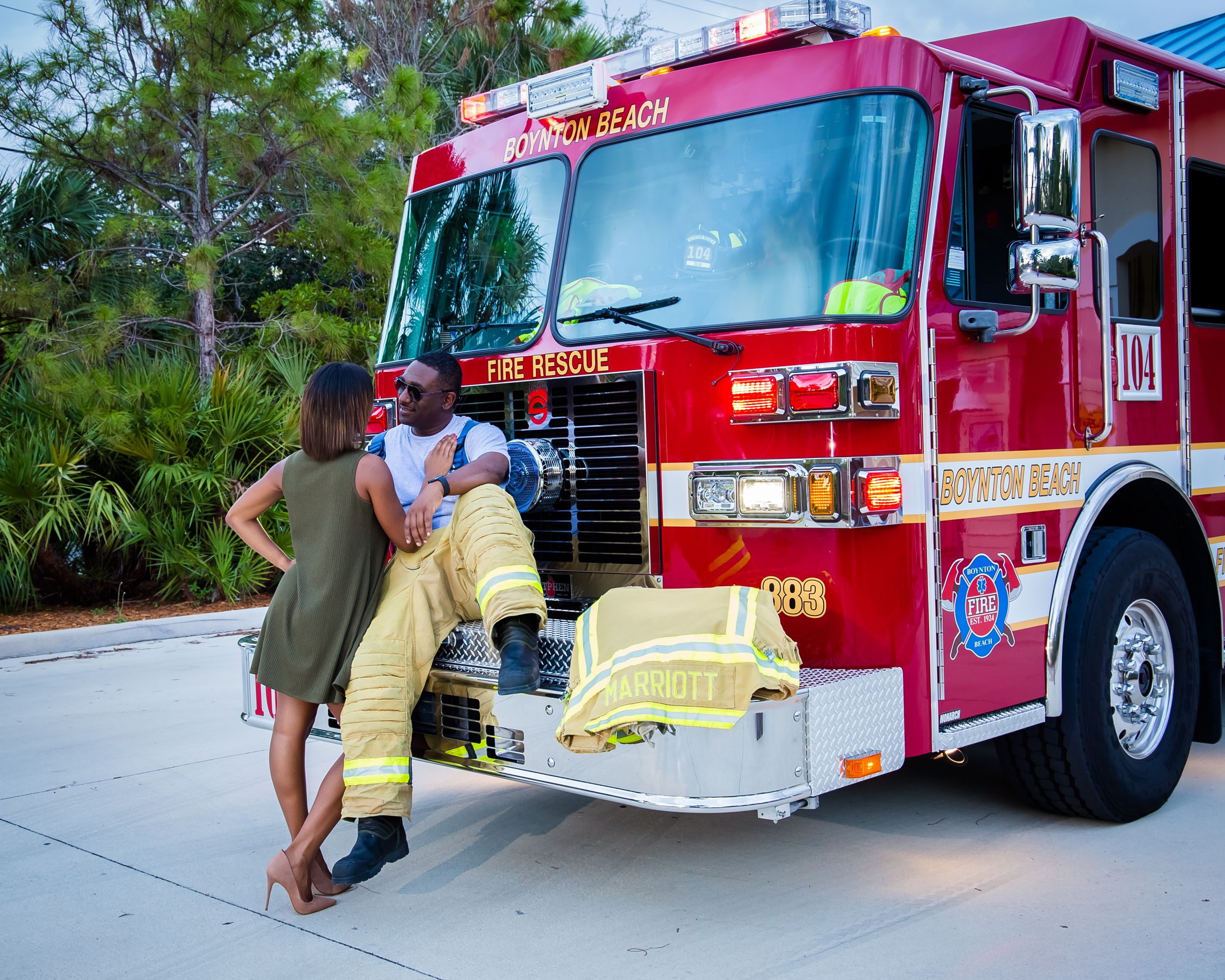 A person in a dress and firefighter interact near the front of a red fire engine.