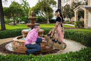 Two people sit together on the edge of a stone fountain in a manicured garden.