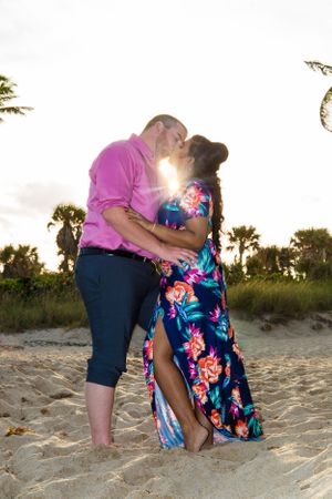 A couple embraces on a sandy beach during sunset wearing coordinated pink and floral outfits.