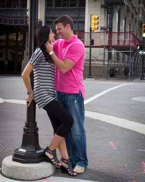 A couple shares an intimate moment by a decorative lamp post on a city street corner.