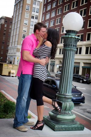 A tender moment shared between a couple next to an ornate street lamp in an urban setting.