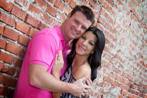 A happy couple embraces against a rustic brick wall background.