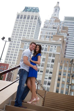 A couple poses on steps with historic architecture and tall buildings in the background.