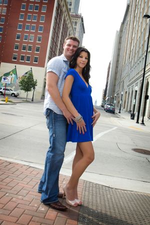 A couple poses together on a city sidewalk with tall buildings in the background.