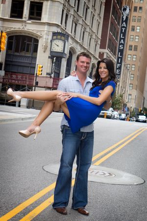 A couple poses playfully in the middle of a city street with vintage buildings in background.