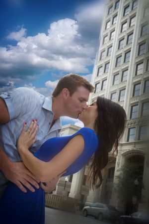 A romantic dip kiss pose in front of an urban building with dramatic clouds.