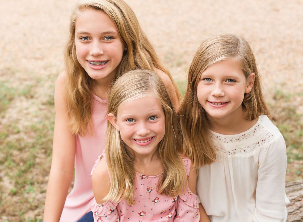 Three young friends with long hair smiling and posing together in a sunny field.
