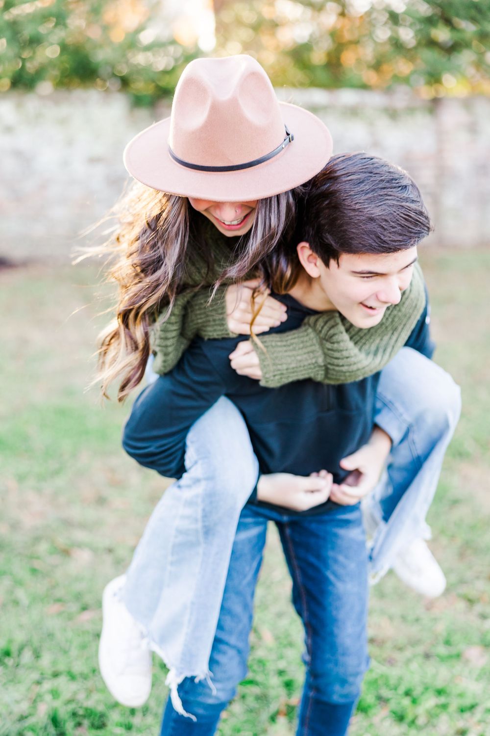 Couple in casual fall attire sharing playful piggyback ride moment outdoors.