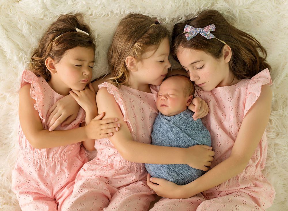 Siblings in pink dresses sleeping peacefully together with a newborn baby in blue.