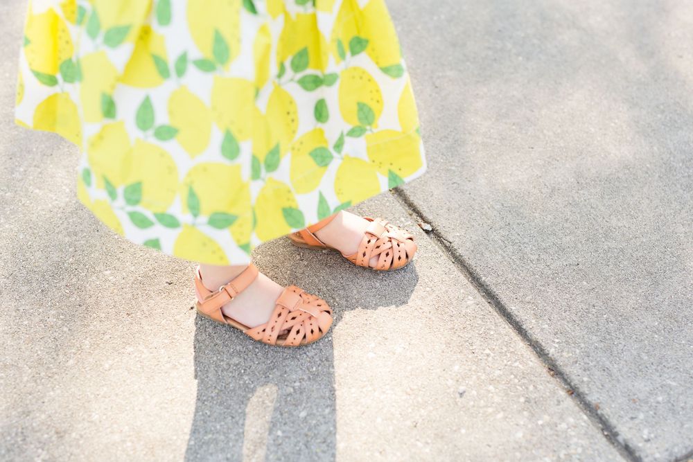 Pink sandals casting a shadow on concrete with yellow floral art in the background.