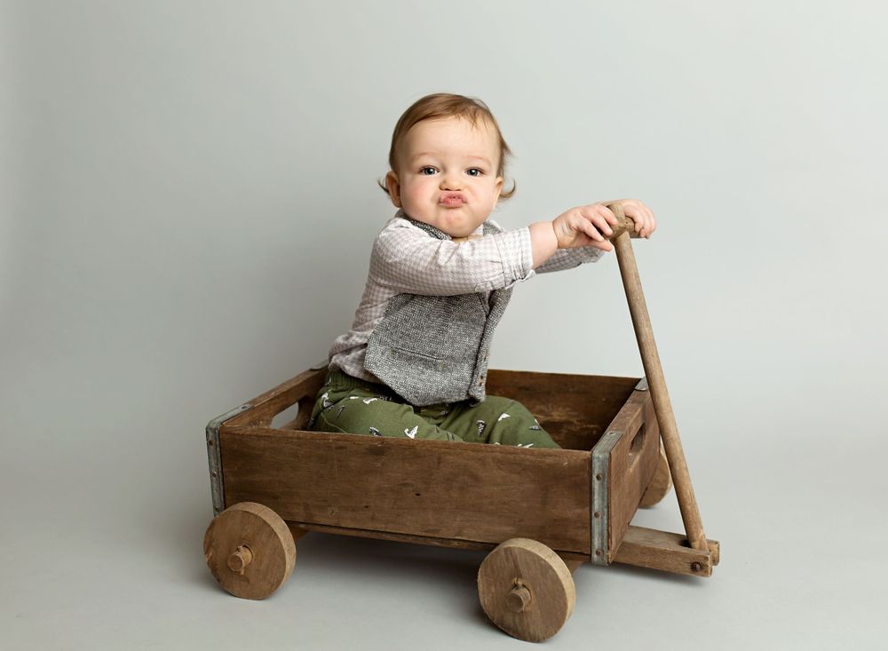 Baby sitting in vintage wooden wagon wearing gray sweater.