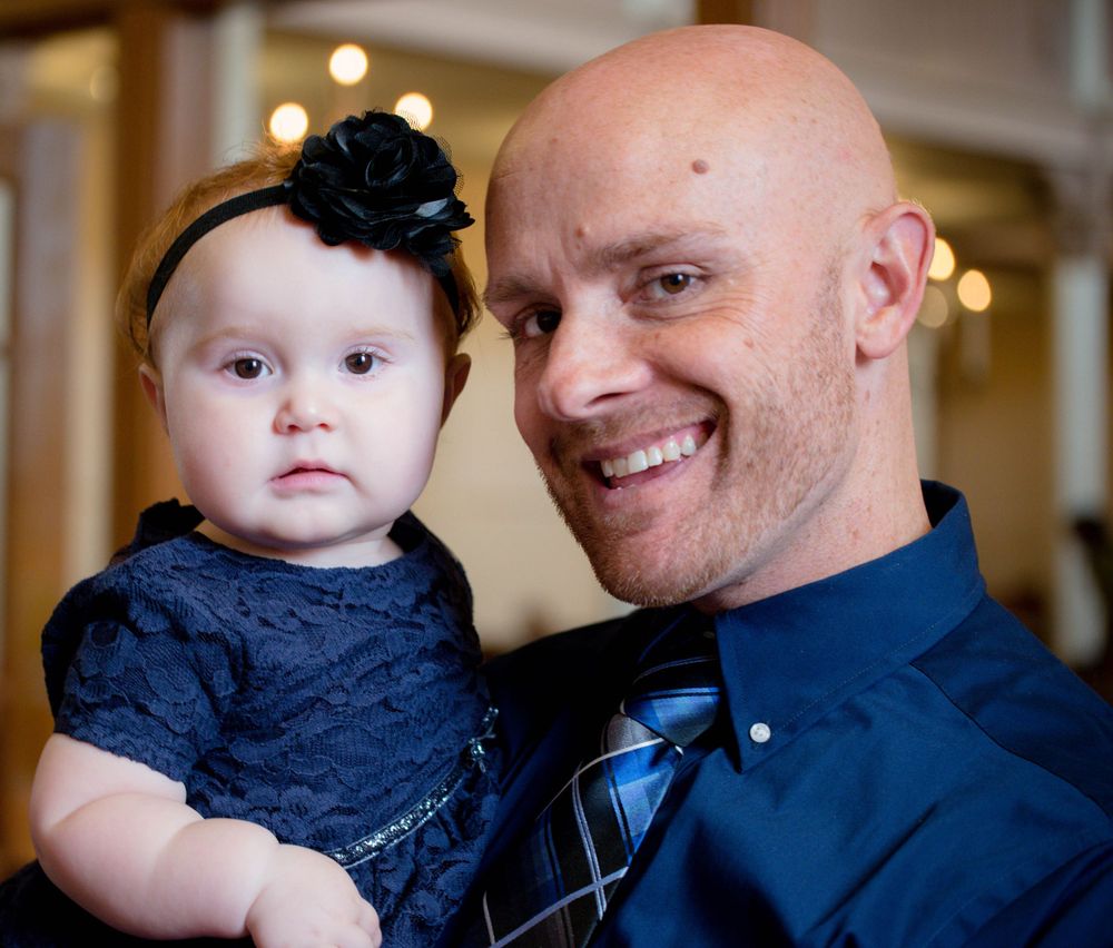 Parent holding small baby wearing navy dress with black flower headband.