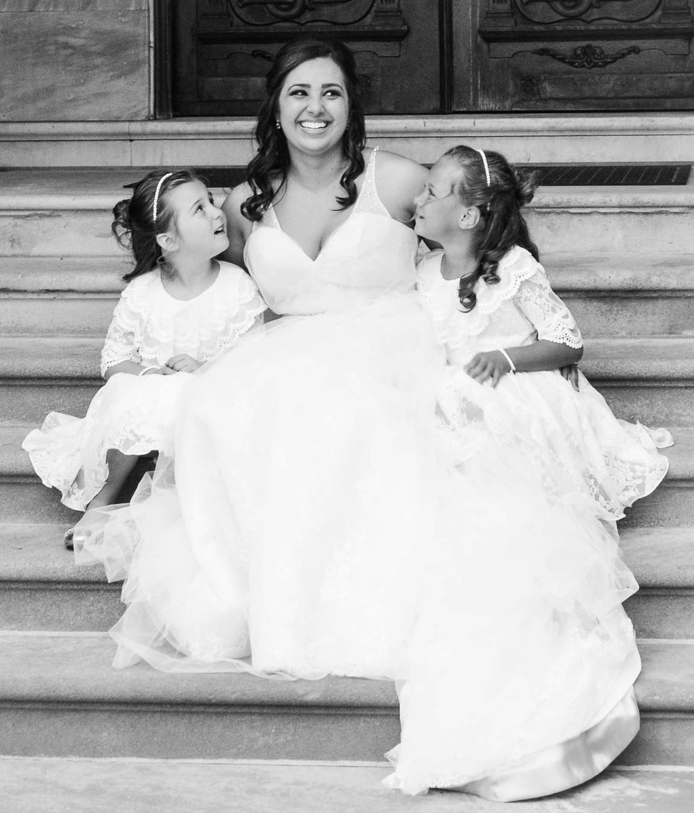 A black and white photo of three people in white dresses sitting on stone steps.