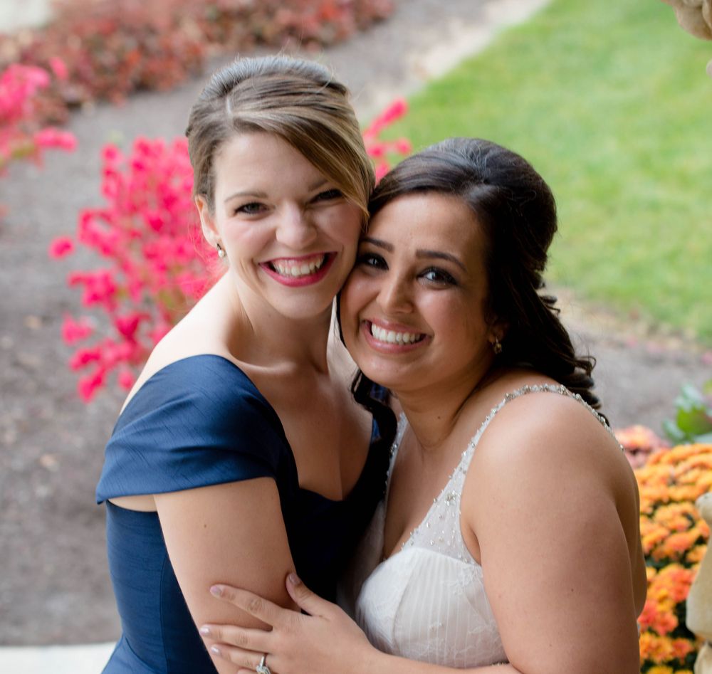 Two people embracing outdoors with bright pink flowers and orange marigolds in the background.