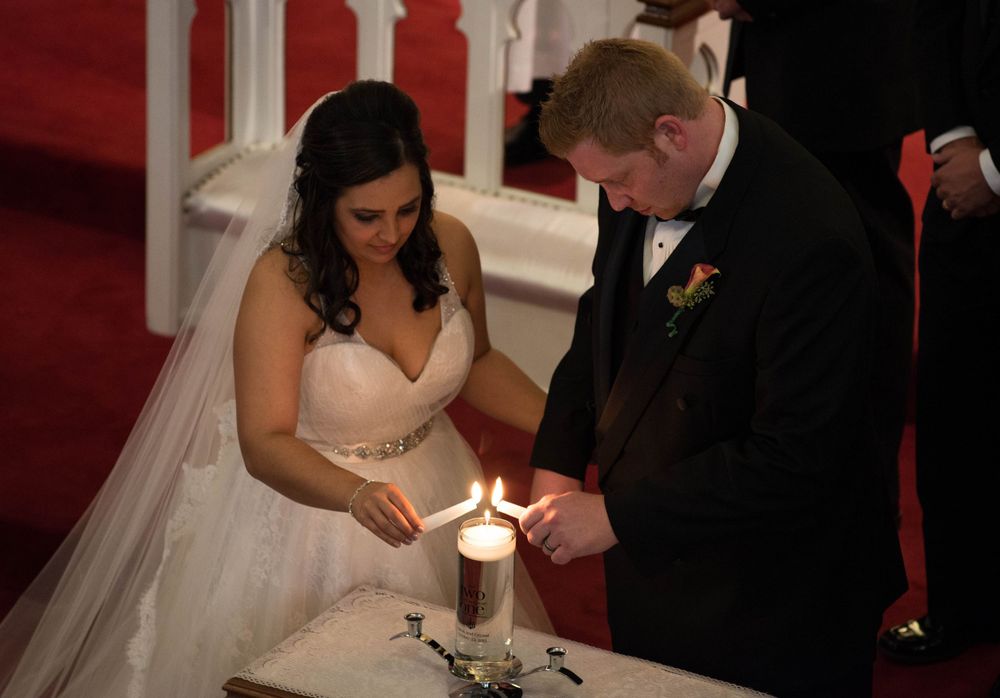 Bride and groom lighting unity candle during church ceremony.