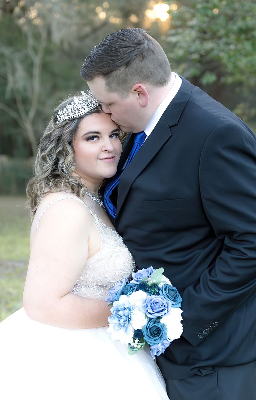 Wedding couple embracing outdoors with bride holding blue roses and wearing a crystal crown.