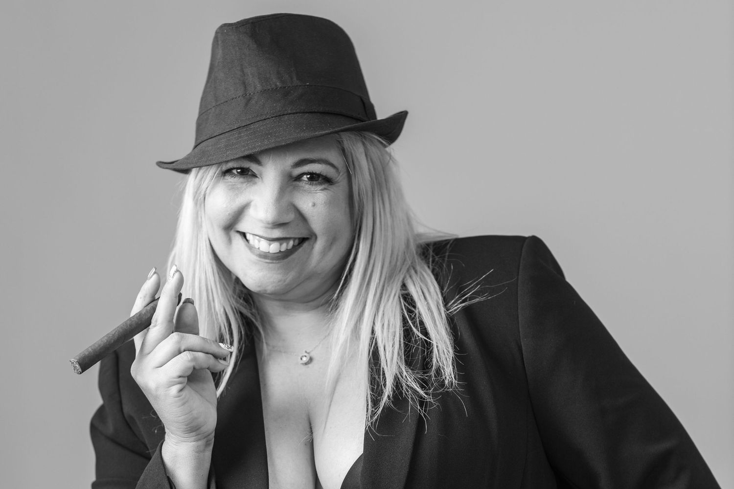 Portrait of person in black blazer and fedora hat against grey background.