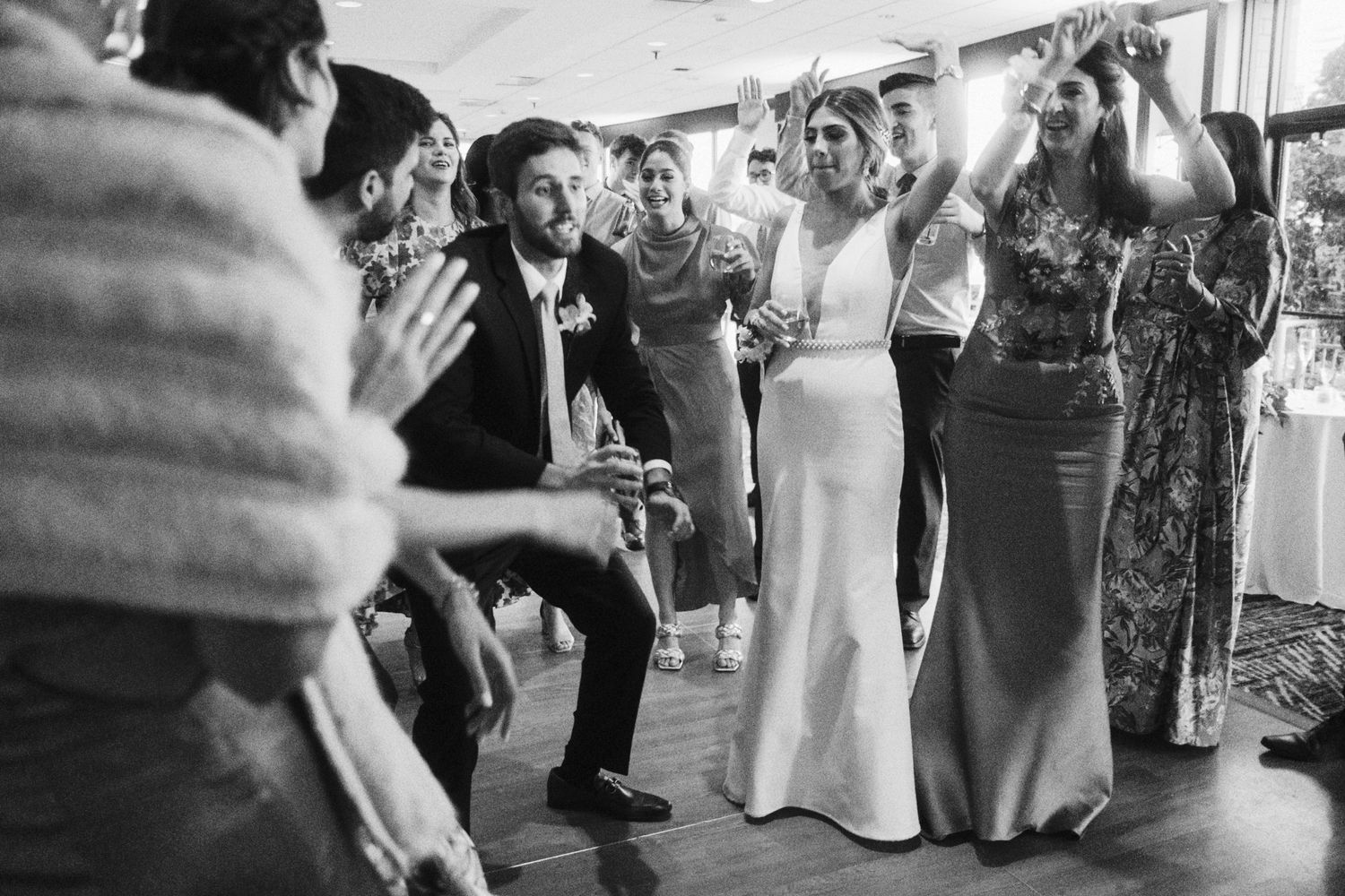 Black and white photo of wedding guests dancing and celebrating at a reception.