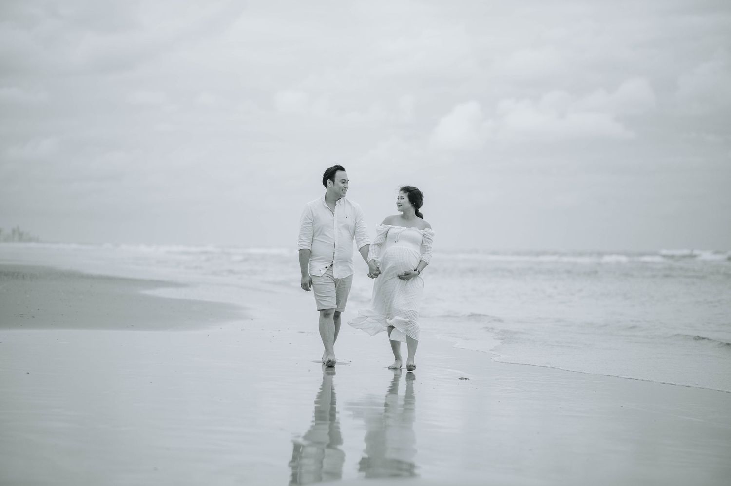 A couple stands together on a misty beach in black and white.