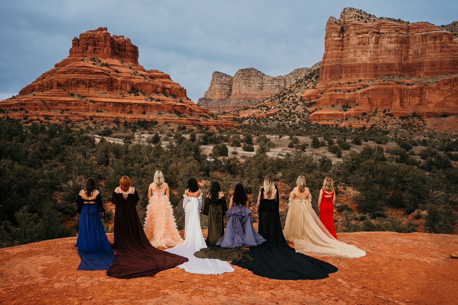 Rainbow of formal gowns lined up against stunning red rock mountain backdrop.