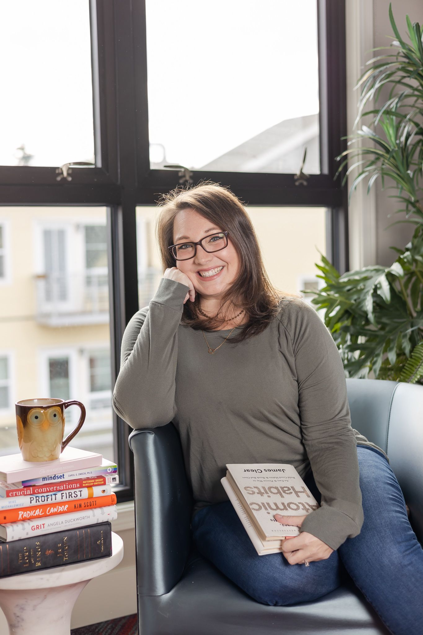 woman sitting on chair with pile of book next and Atomic Habits in lap for headshots in Woodinville, WA