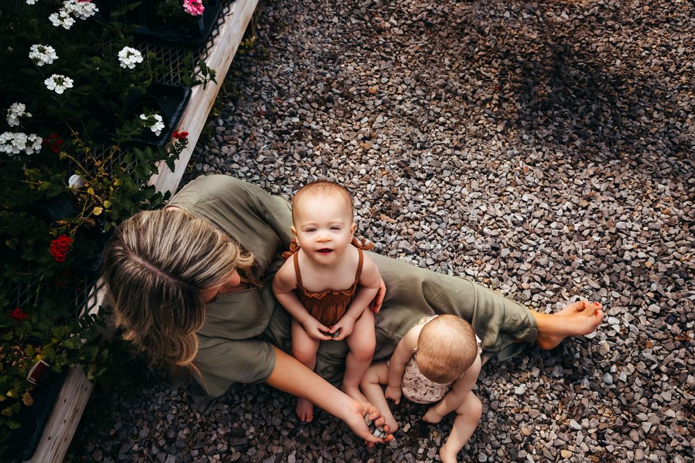 A mother and baby play together while lying down outdoors on a bed of dried leaves.
