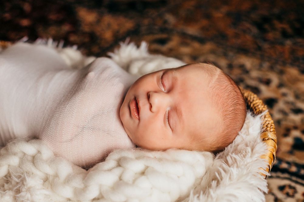 A sleeping newborn baby wrapped in white lies on soft textured fabric.