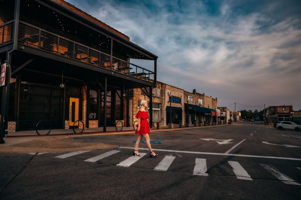 Person in red dress crossing a zebra crossing in front of a historic downtown storefront at dusk.